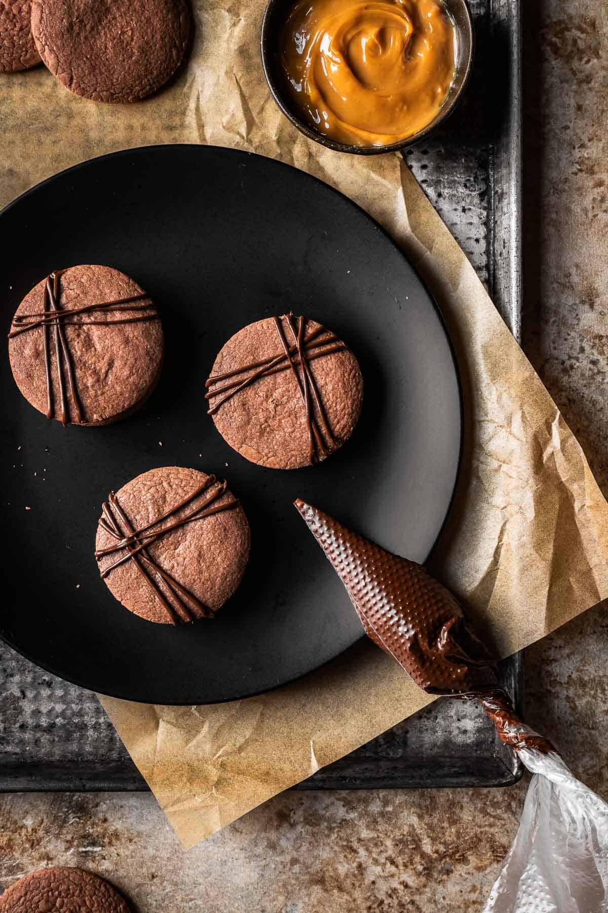 Three cookies on a black plate with piped stripes of chocolate on top.