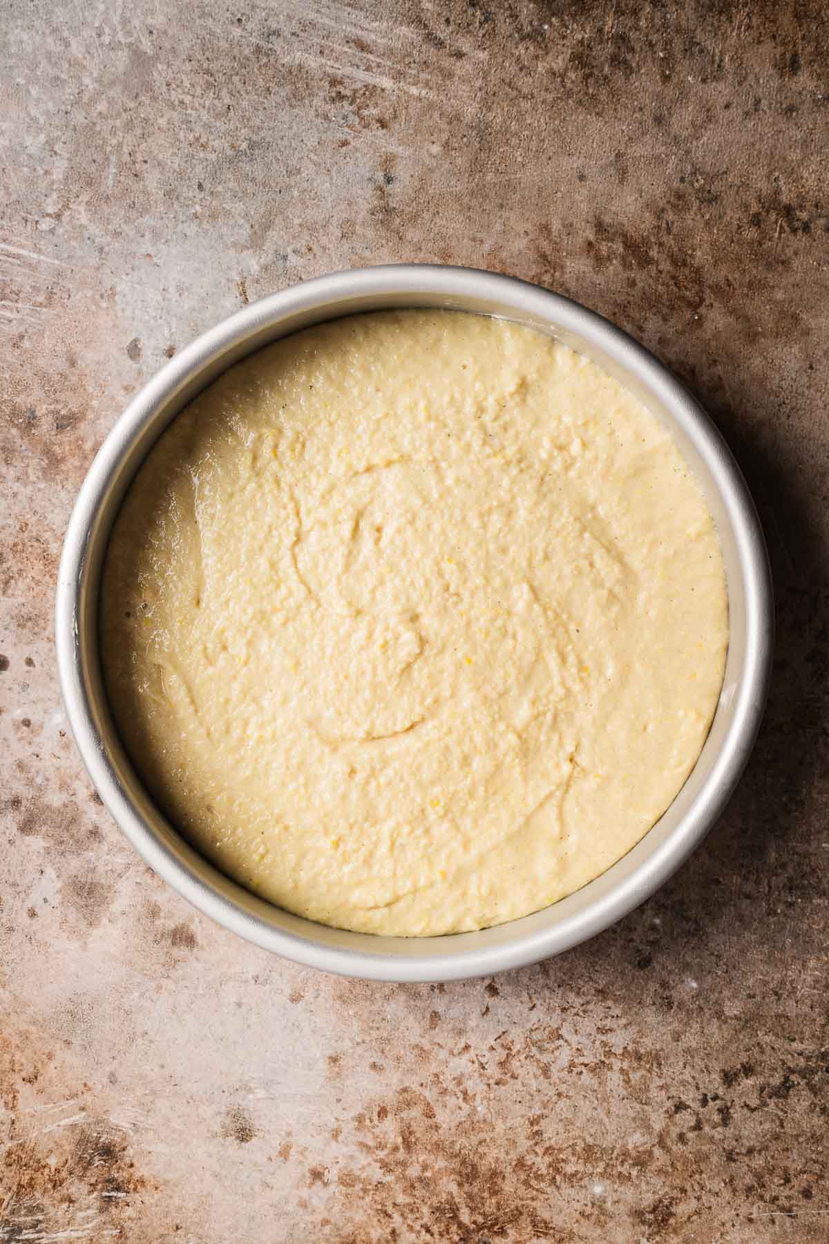 Cake batter sprinkled with granulated sugar in a round metal pan.